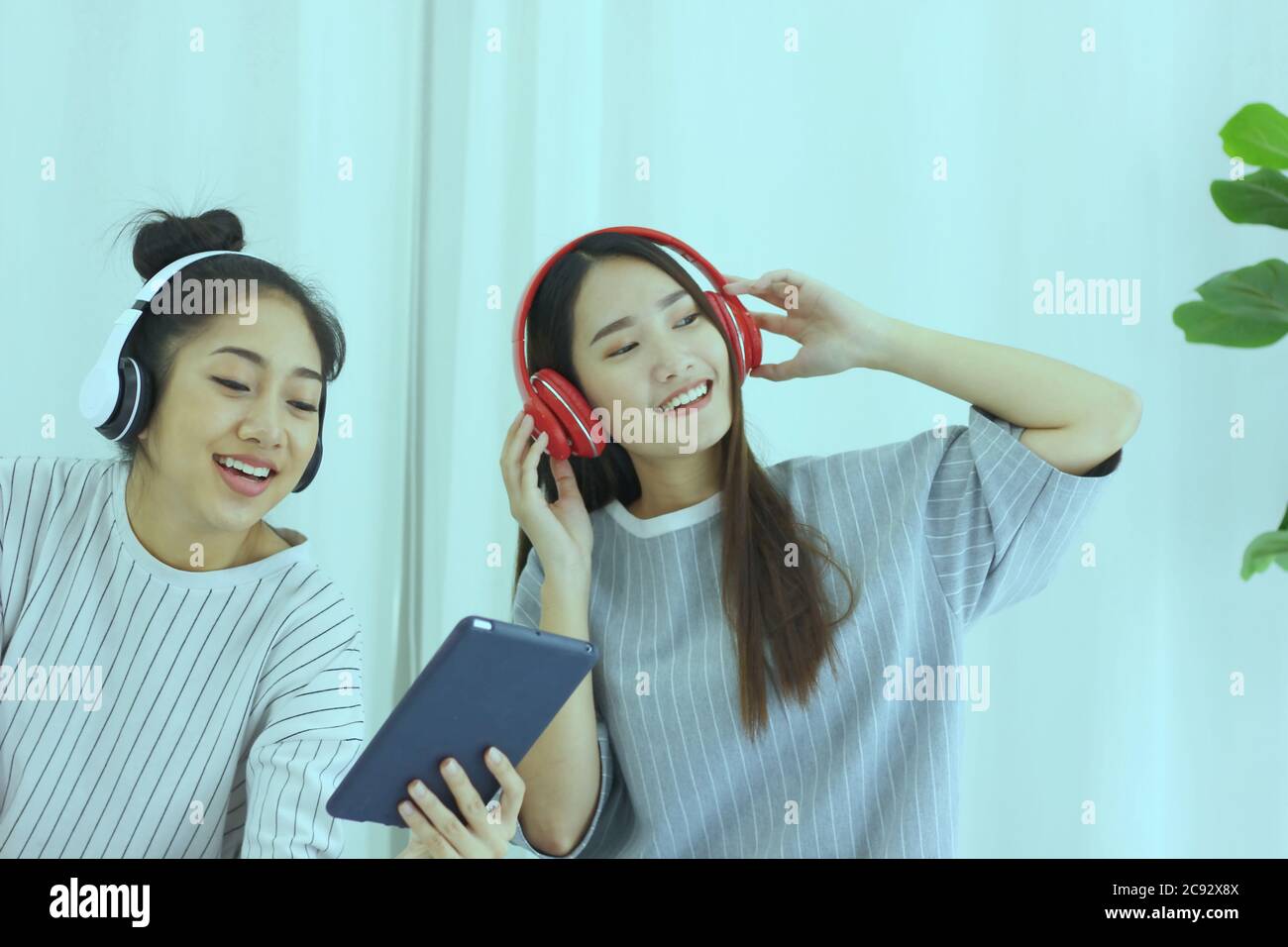 Dos adolescentes asiáticos en el momento feliz con la música del amor Iliving room. Los adolescentes que usan la tableta con los auriculares disfrutan con la hermosa música Foto de stock