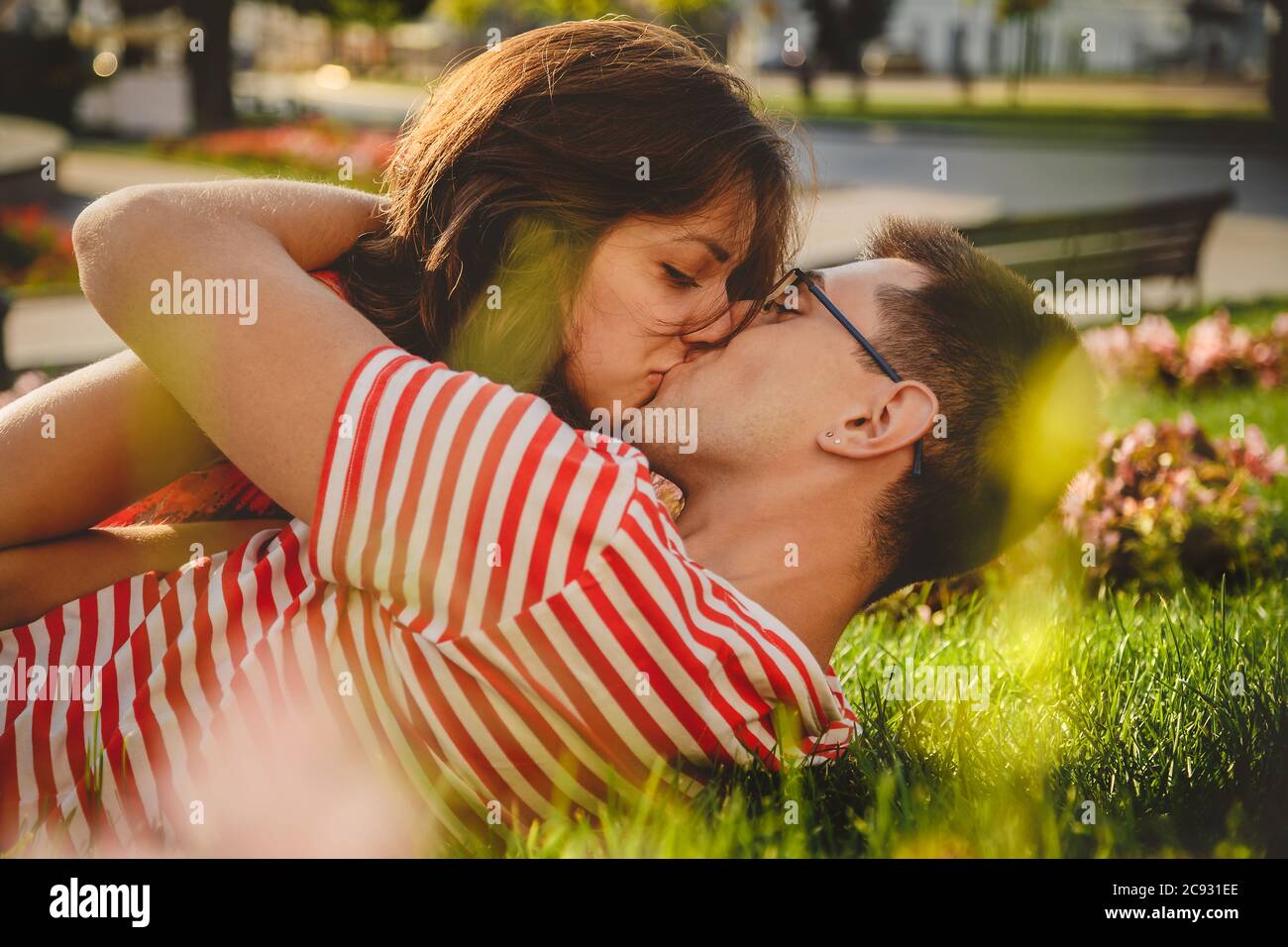 Una pareja encantadora tumbada en césped verde en el parque, besándose y pasando tiempo juntos Foto de stock