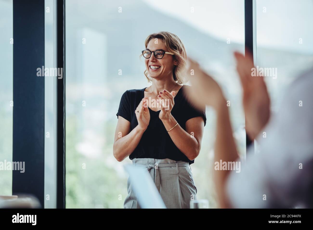 Una mujer de negocios que se alzaba las manos después de una sesión exitosa de lluvia de ideas en la sala de juntas. Gente de negocios mujeres aplaudiendo después de reunión productiva. Foto de stock