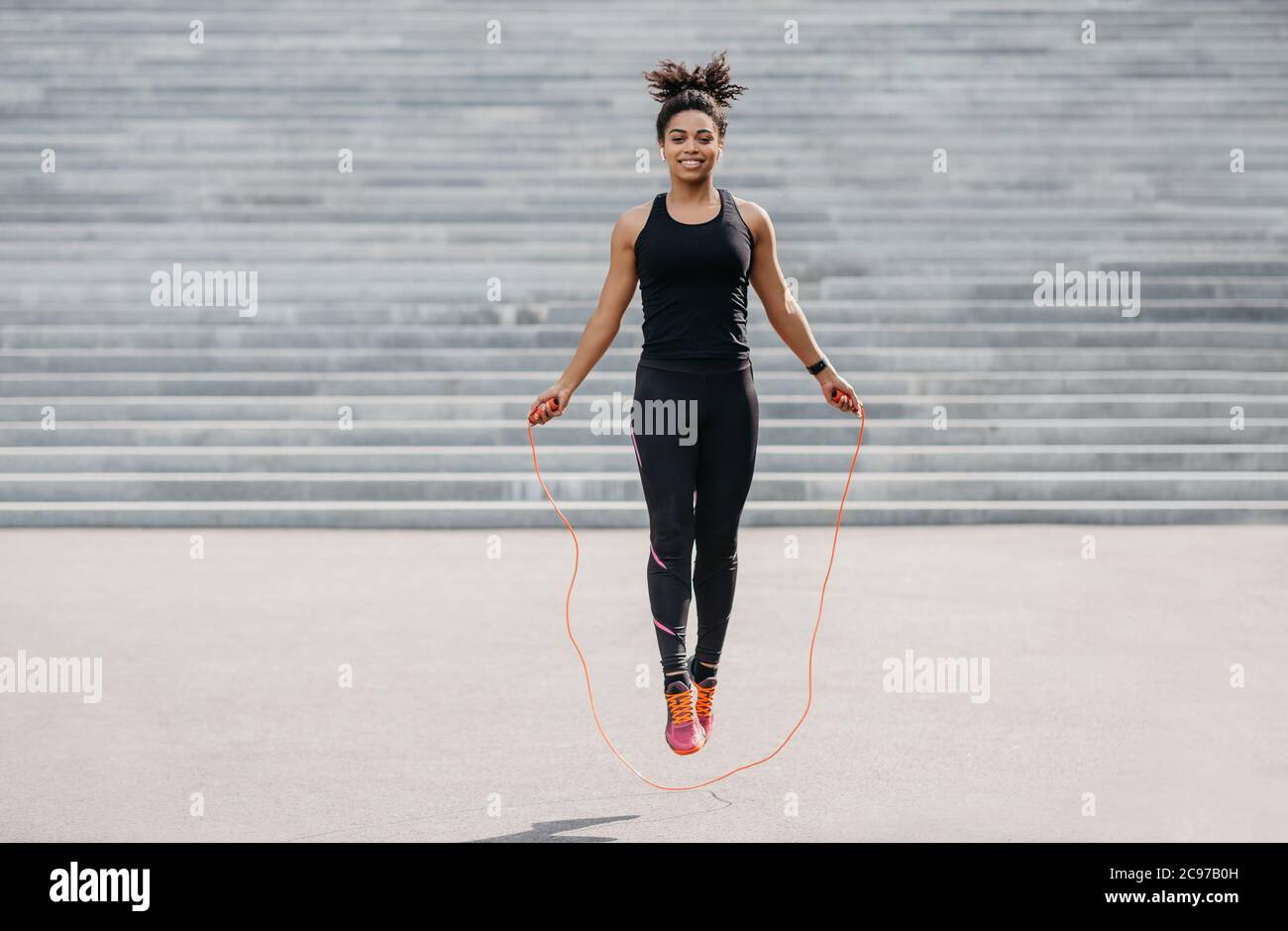 La atleta femenina hace ejercicio cardiovascular. Chica sonriente en sportswear con fitness tracker saltar cuerda Foto de stock