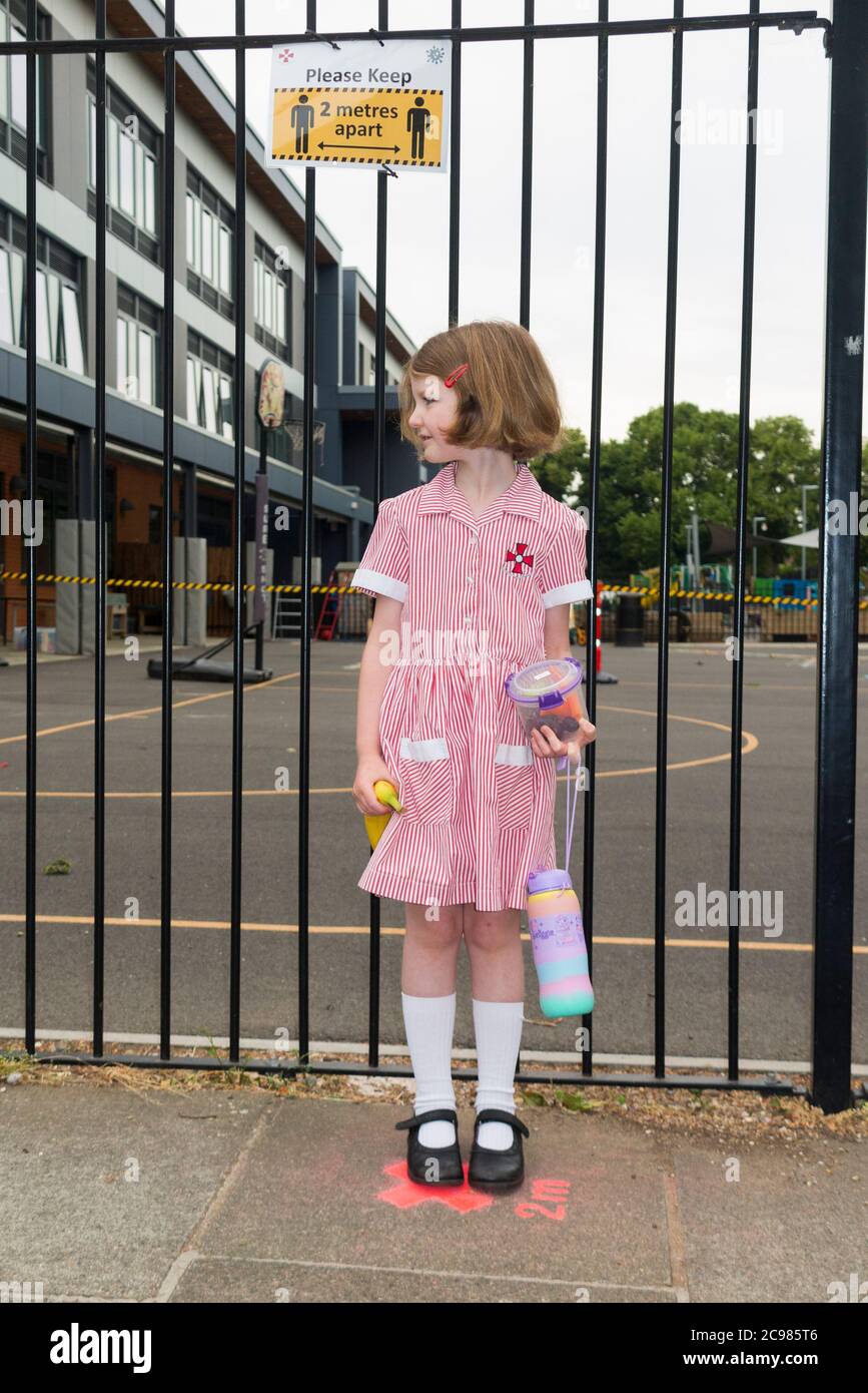 Una niña de seis años de edad, estudiante o estudiante hace cola en la entrada de su escuela de una manera socialmente distanciada a 2 m de otros alumnos de la escuela. Inglaterra Reino Unido (119) Foto de stock