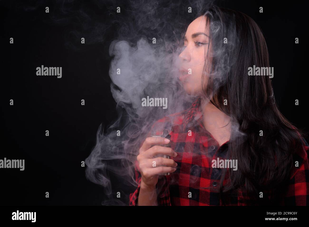 Joven hermosa mujer asiática vaping contra fondo negro Foto de stock