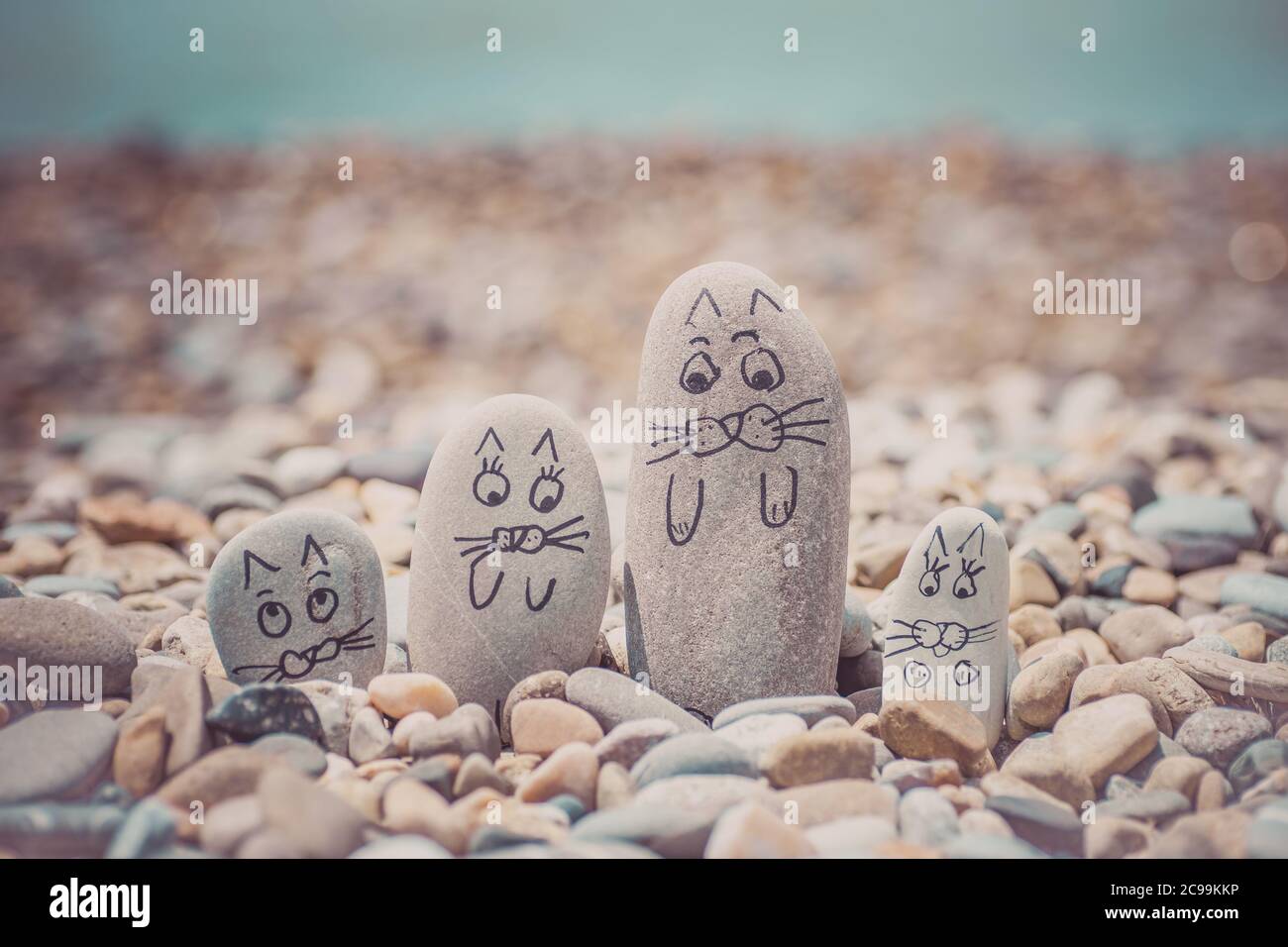 Guijarros con caras dibujadas en la arena. Padre, madre, hija e hijo. Familia de gatos concepto de vocación Foto de stock