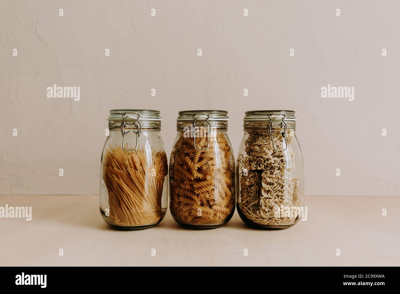 Tres recipientes de jarra de cristal llenos de ingredientes secos no cocidos. Arroz, pasta, harina, azúcar. Foto de stock