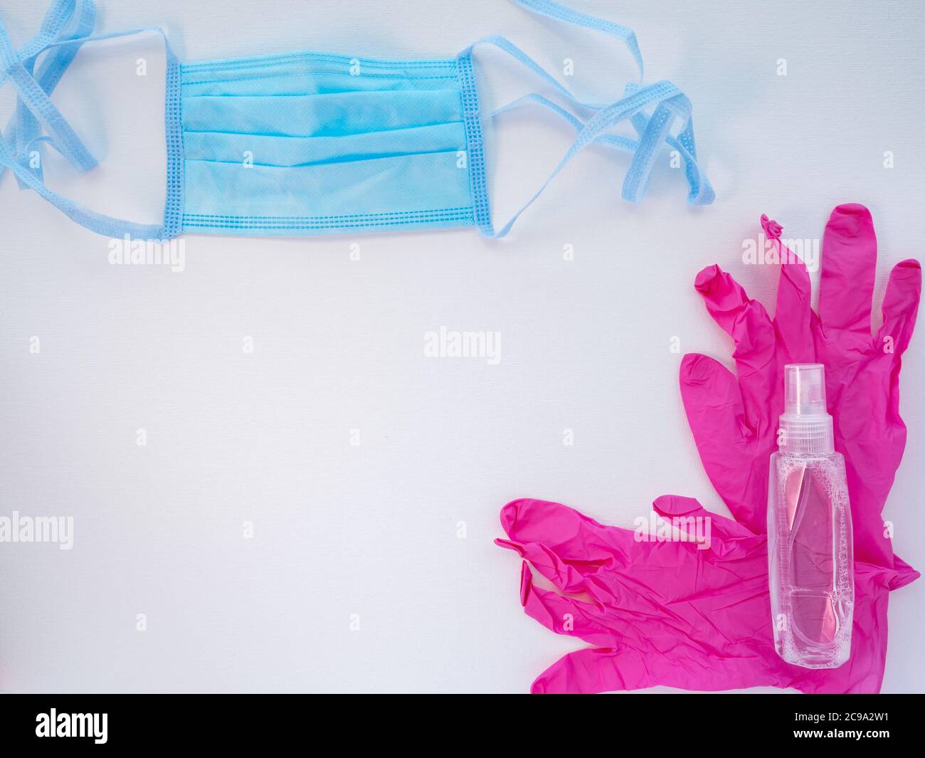 Máscara facial médica protectora azul, un par de guantes de látex rosa y una botella de desinfectante de manos sobre fondo blanco. Protección antiviral durante el covid. Foto de stock
