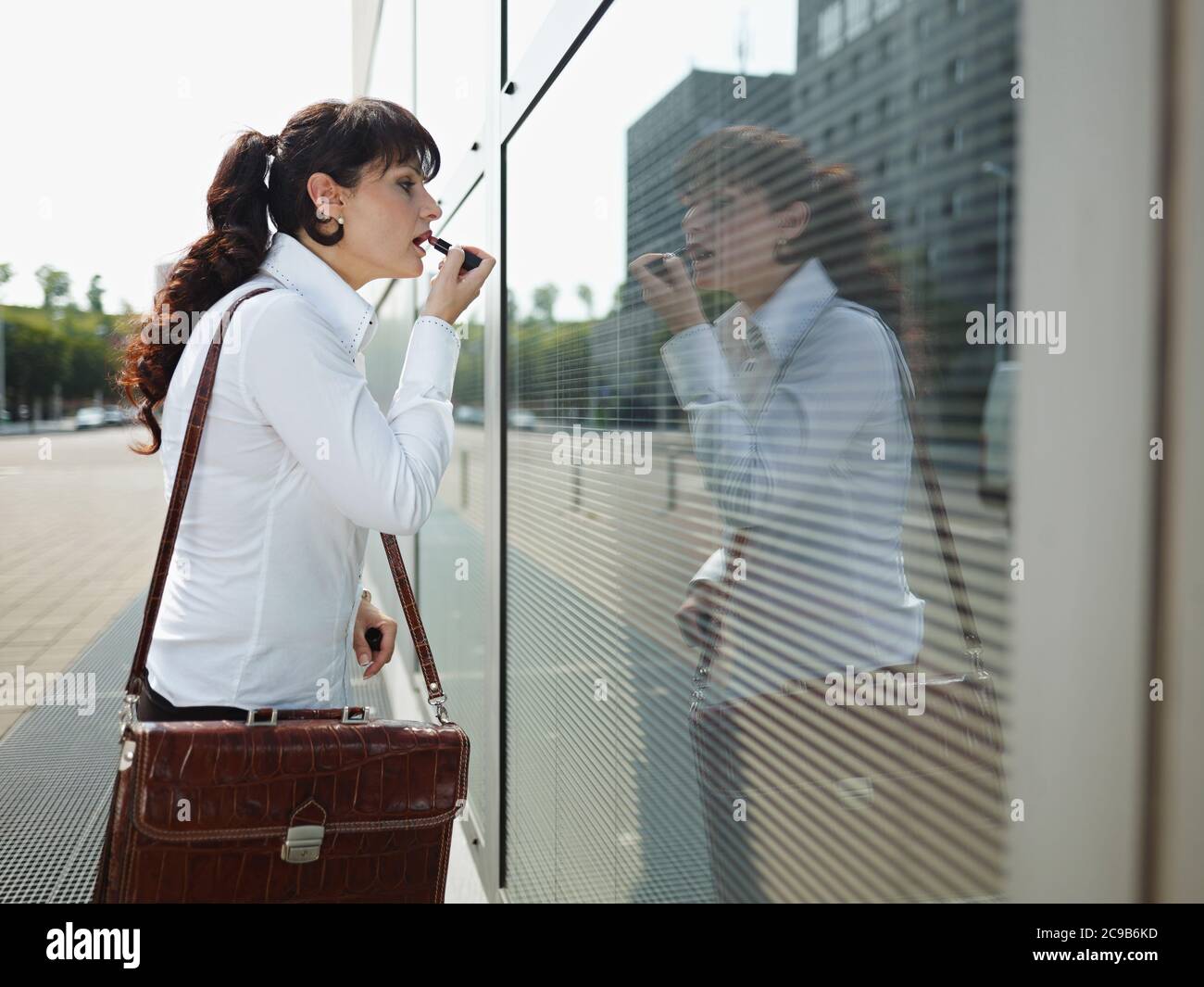 Mujer de negocios aplicando maquillaje Lipstick en la calle utilizando Office Window Foto de stock