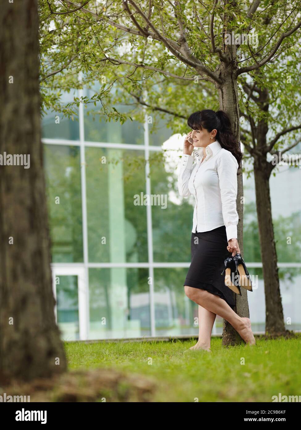 Mujer madura de pie en hierba Barefoot durante la llamada de negocios Foto de stock
