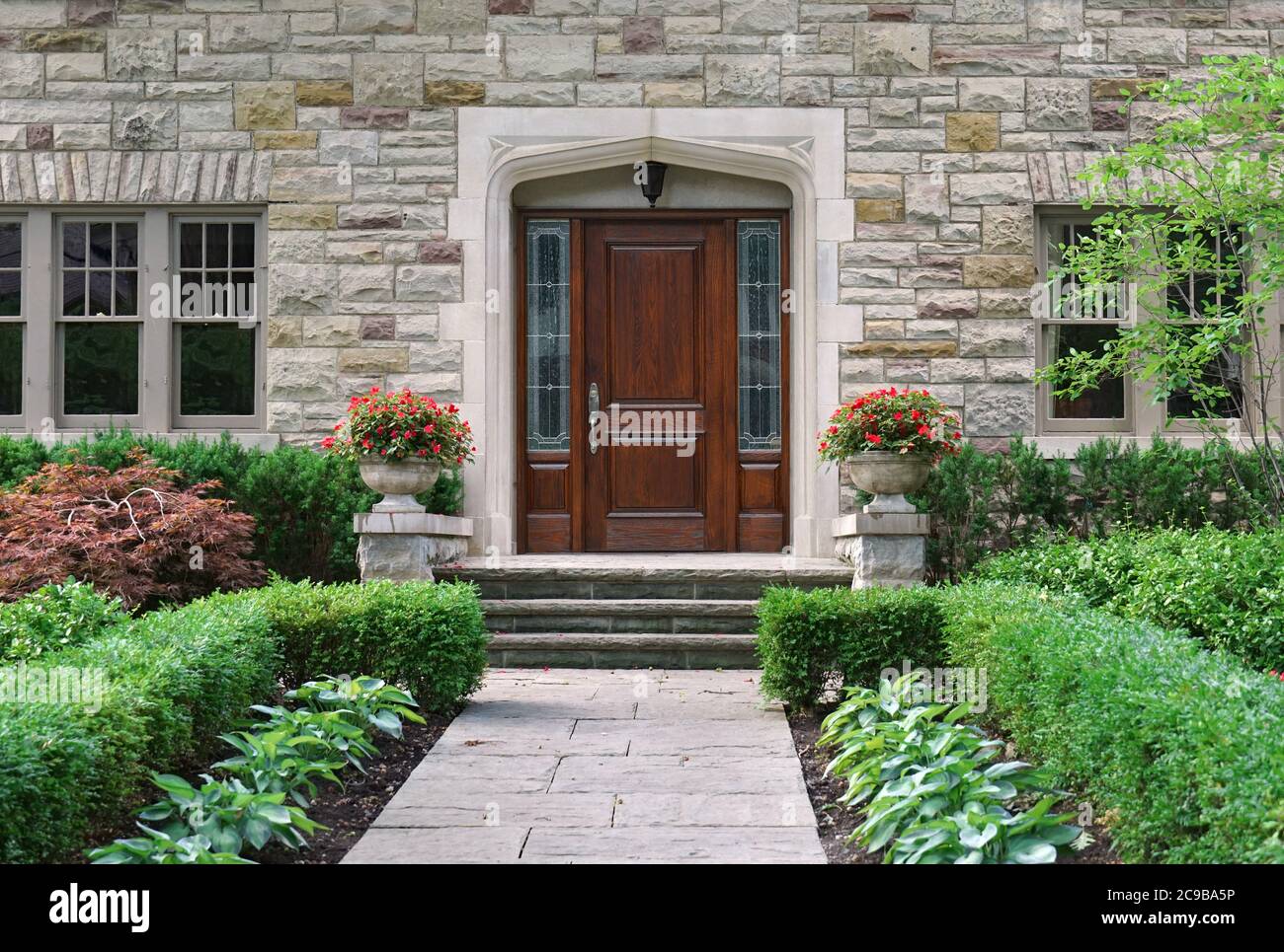 Casa con frente de piedra con arbustos y elegante puerta frontal de madera con manjares Foto de stock