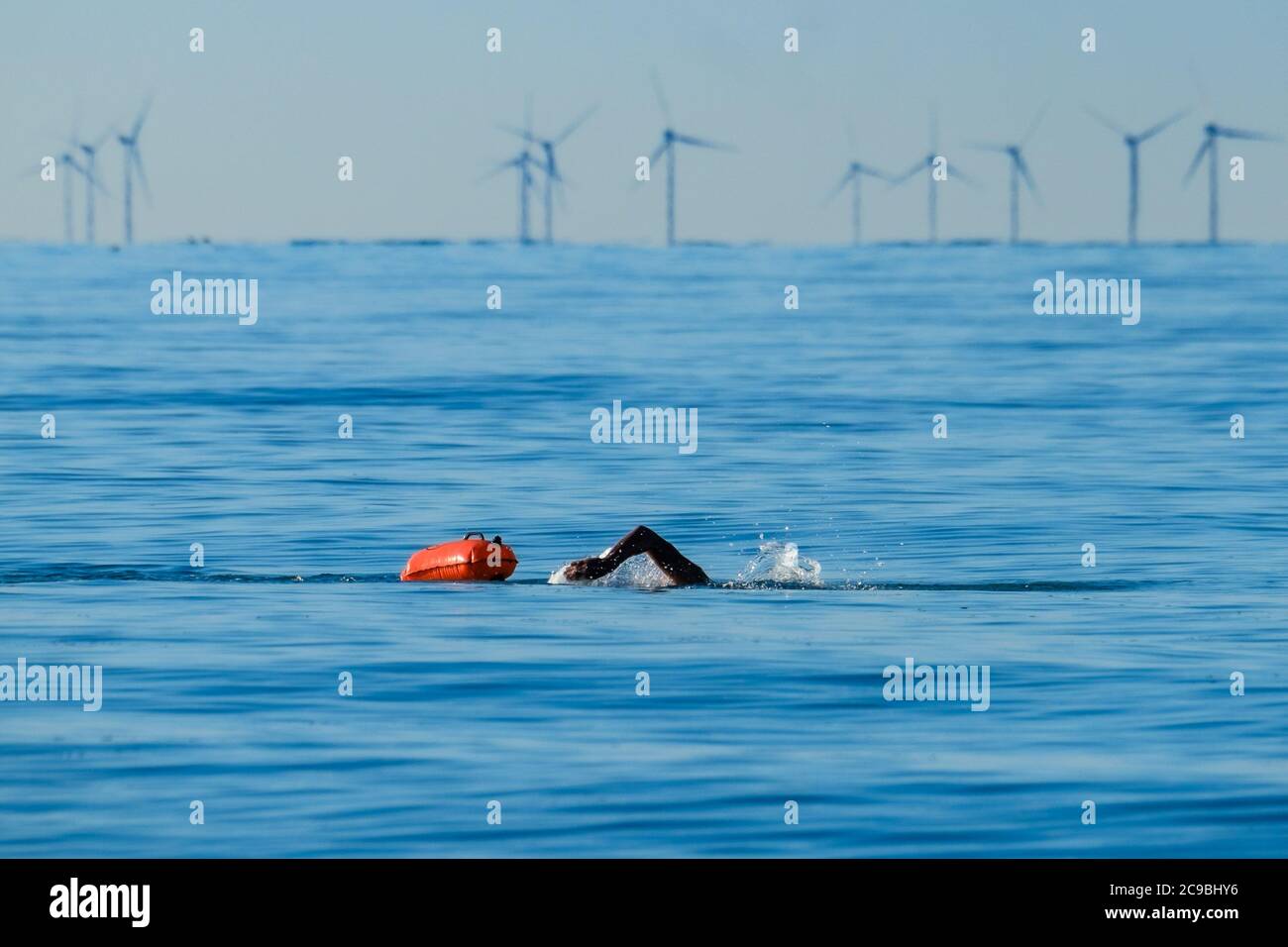 Worthing Beach, Worthing, Reino Unido. 30 de julio de 2020. Los nadadores de agua abierta disfrutan del mar tranquilo de la mañana. Con un cielo azul claro y aguas planas la gente en tablas de paddle disfrutar de la mañana temprano en la costa de sussex. El Parque Eólico Rampion se puede ver 13-20km costa afuera. Imagen de crédito: Julie Edwards/Alamy Live News Foto de stock