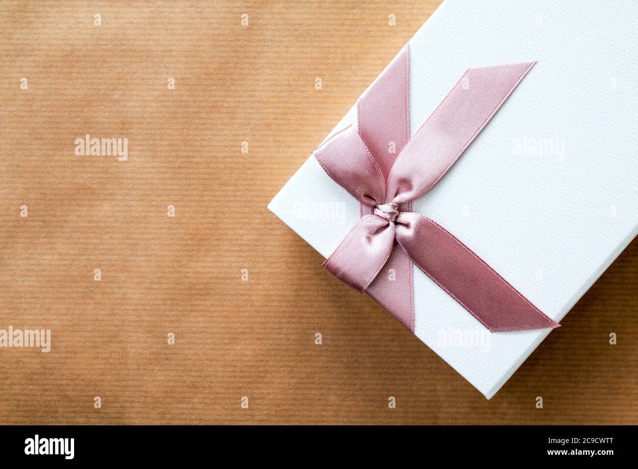Caja de regalo blanca decorada con un lazo rosa sobre papel marrón en un  ángulo con espacio de copia para mensajes personalizados Fotografía de  stock - Alamy