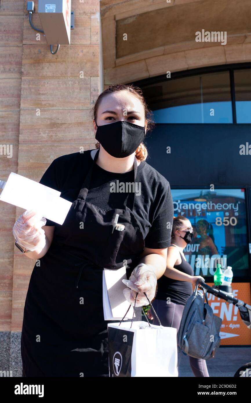 Una camarera enmascarada y enamecida que lleva una orden de comida al coche desde el Café Latte para el servicio al lado de la acera. St Paul Minnesota MN EE.UU Foto de stock