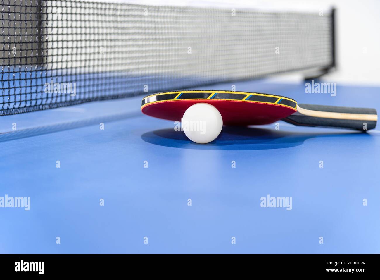 Tapeta roja de tenis de mesa y una pelota blanca en la mesa de ping pong azul con una red negra, la paleta de tenis de mesa es un equipo de competición deportiva i Foto de stock