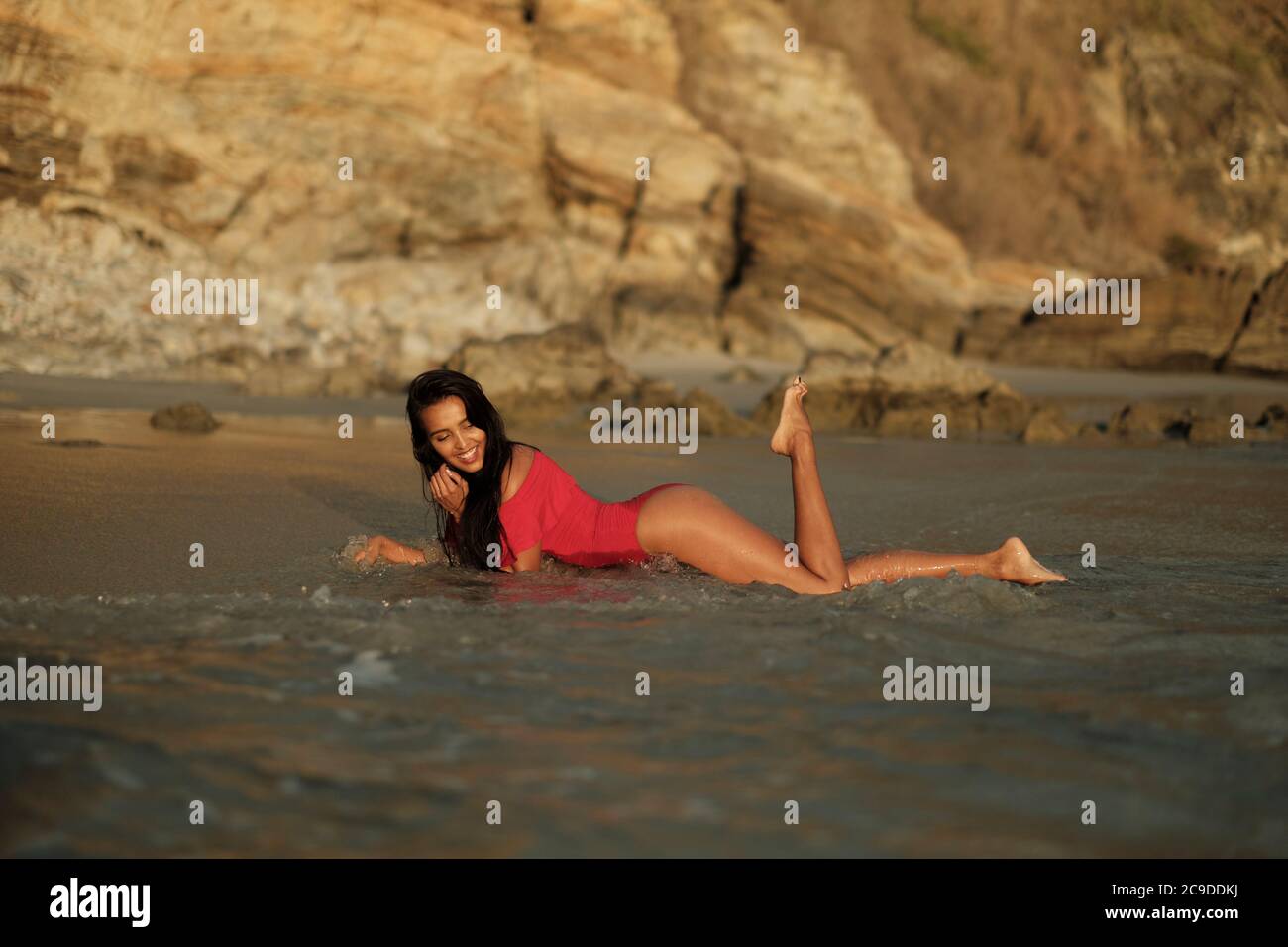 Mujer latina joven en traje de baño rojo disfrutando del surf en Una playa rocosa en la costa del Pacífico de México Foto de stock