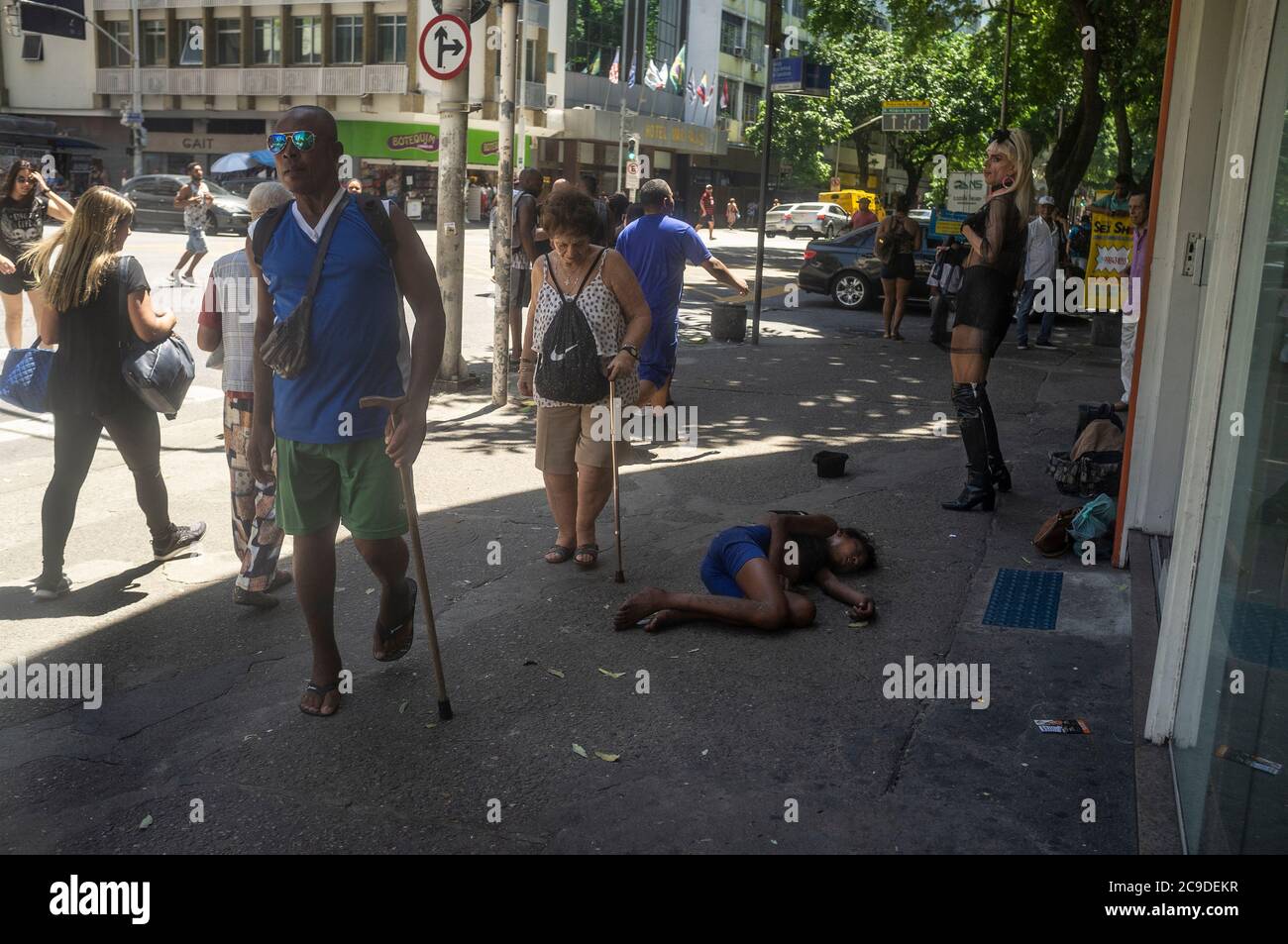 Vida cotidiana en el barrio de Copacabana, los peatones que usan bastones de caminar pasan por un espectáculo de travestis y un débil niño de la calle durmiendo en el suelo. Foto de stock