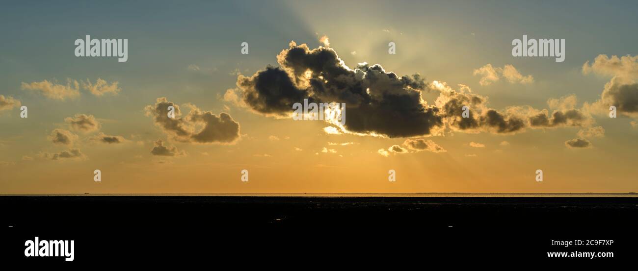 Nubes con rayos de sol durante la puesta de sol sobre el mar de Wadden en la costa norte de Holanda. Foto de stock