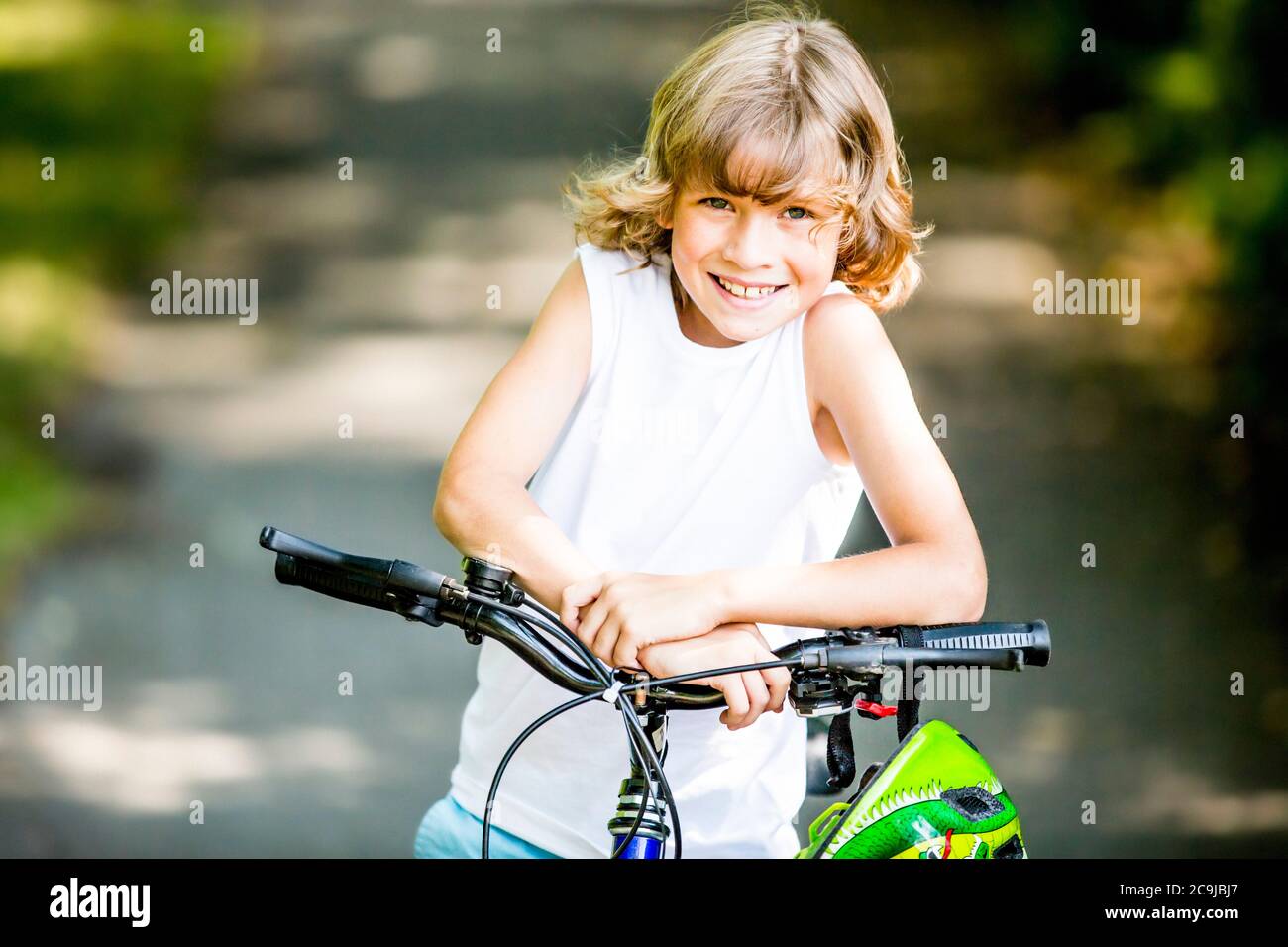 Niño sentado en bicicleta en el parque, sonriendo, retrato. Foto de stock