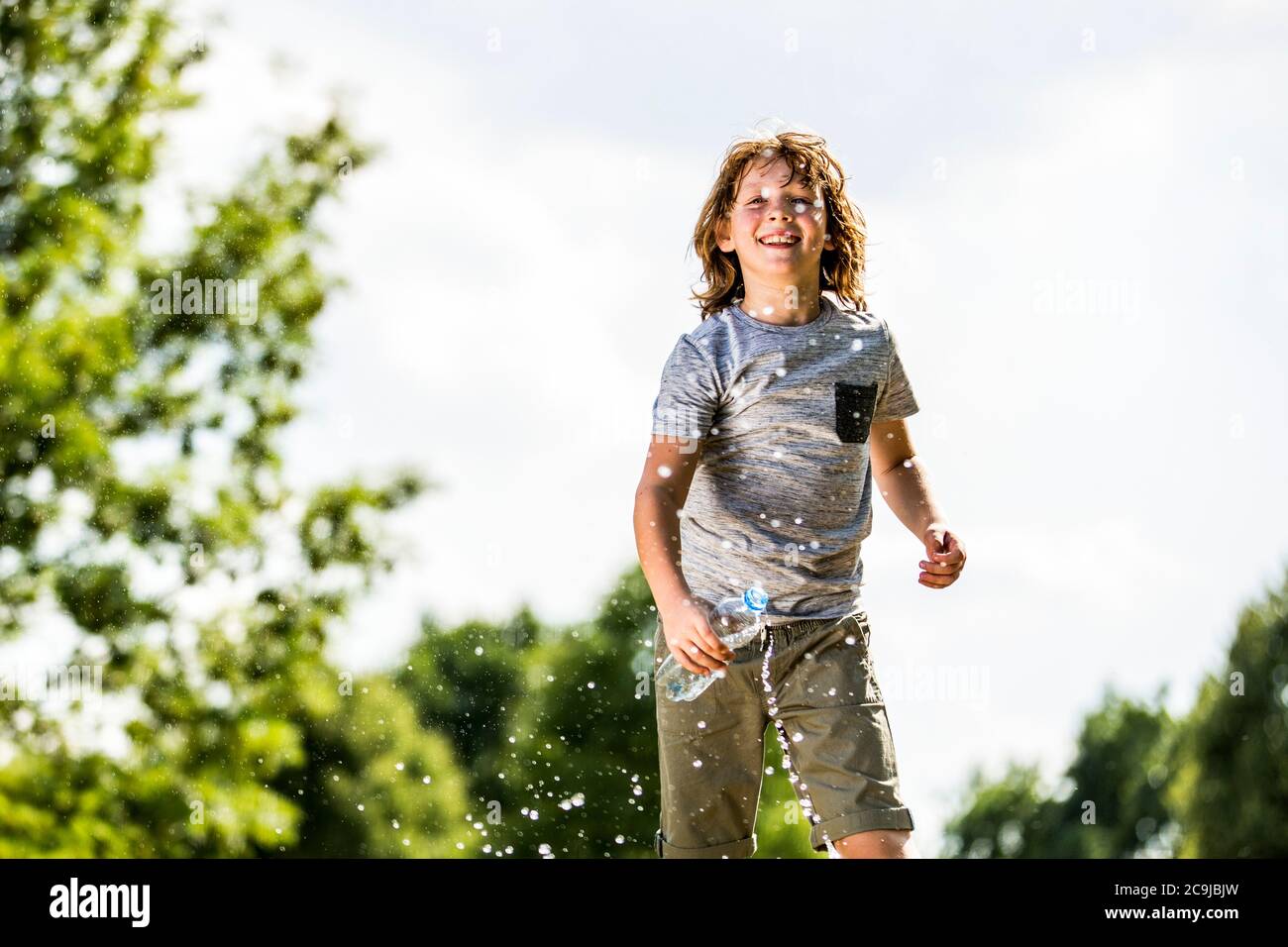 Niño salpicando agua de una botella de plástico, sonriendo, retrato. Foto de stock