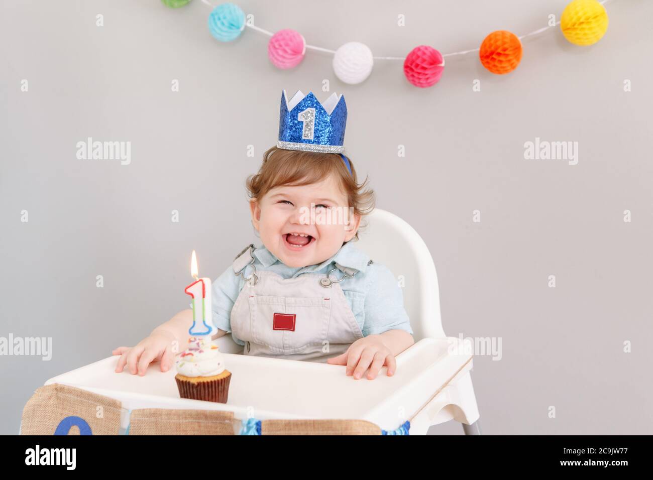 Feliz sonriente lindo bebé caucásico niño en corona azul celebrando su primer  cumpleaños en casa. Niño niño niño niño pequeño sentado en silla alta  comiendo sabrosa taza Fotografía de stock - Alamy