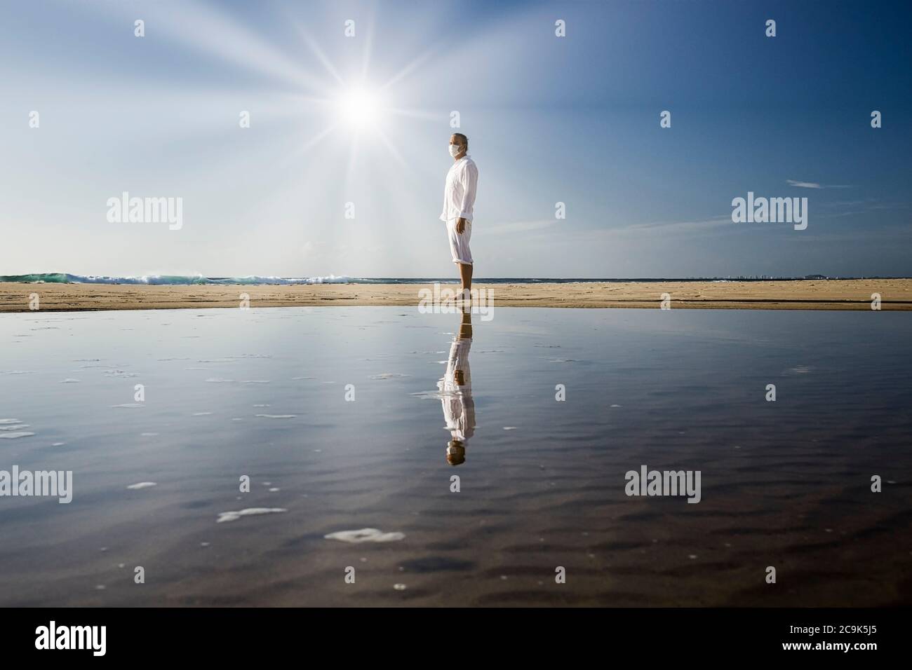 hombre con máscara médica caminando en la playa durante la pandemia del coronavirus covid 19, concepto de distancia social, ejercicio masculino usando máscara para la protección Foto de stock