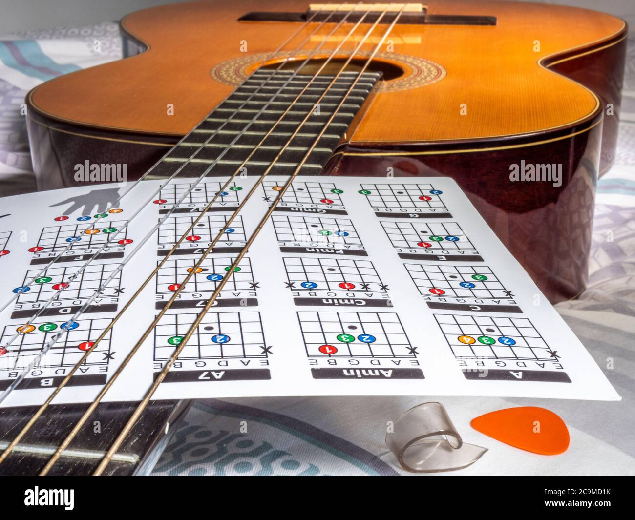 Una tarjeta de acordes para principiantes que se mantiene en su lugar a  través de las cuerdas de una guitarra clásica de nylon, acostada en una cama  después de la práctica Fotografía