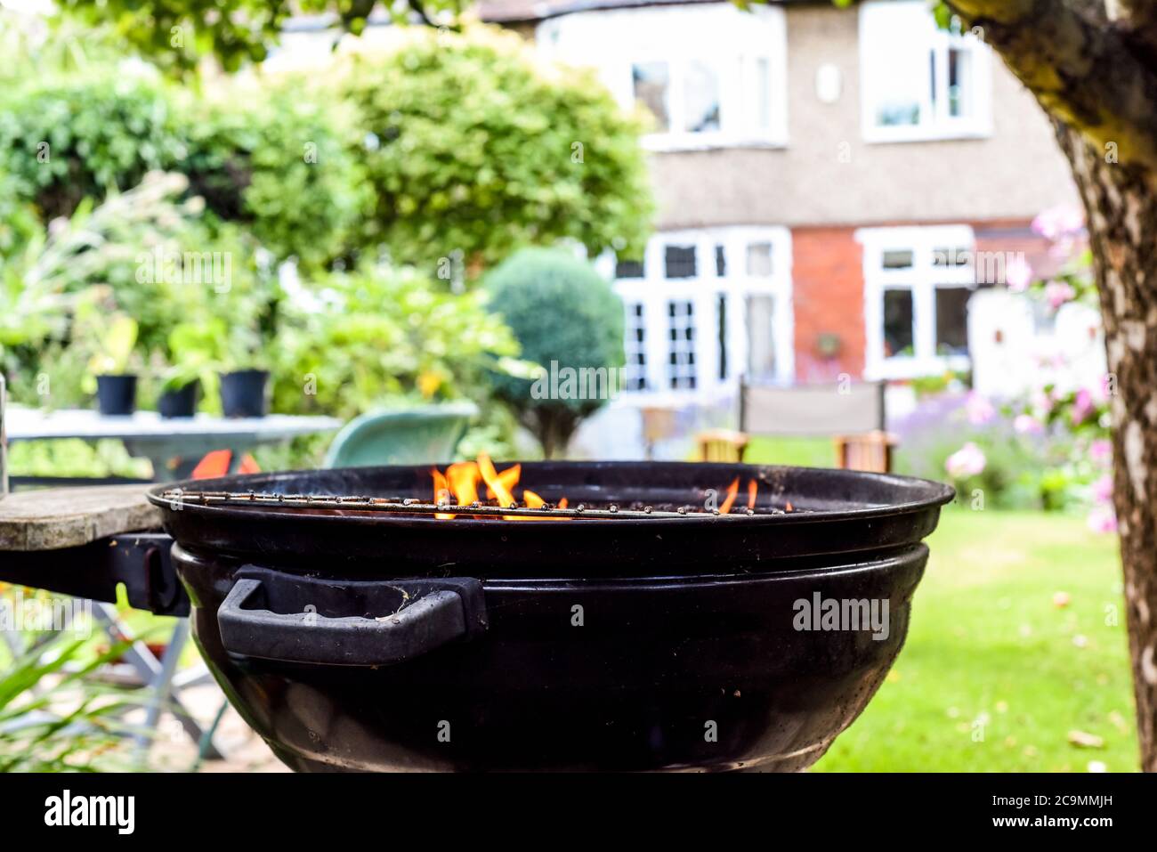 Barbacoa con llamas en un jardín trasero vacío preparándose para cocinar al aire libre Foto de stock