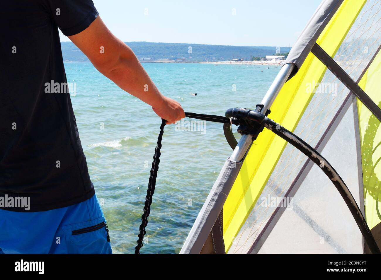 hombre sosteniendo vela de windsurf para cerrar la cuerda Foto de stock