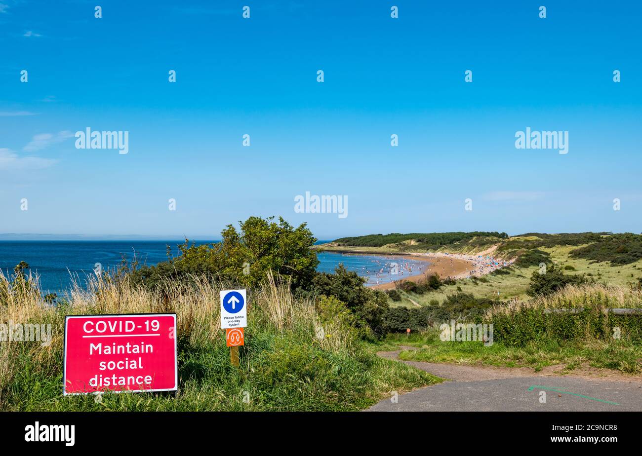 Playa llena de gente con señales de distancia social y de una dirección en el caluroso día de verano durante la pandemia de Covid-19, Gullane, East Lothian, Escocia, Reino Unido Foto de stock