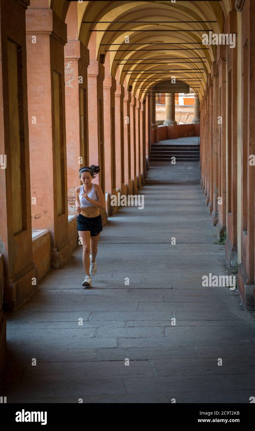 Adolescente en pantalones cortos, sujetador deportivo y zapatillas de deporte con cinta para correr a través del pórtico en Bolonia Italia Foto de stock