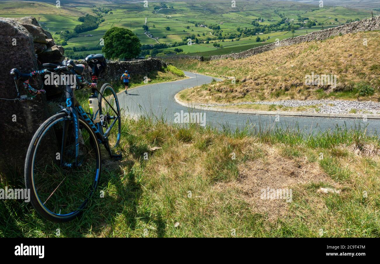 El ciclista se detuvo en el camino hacia abajo atrapando a Hill con un corredor que también se dirigía hacia abajo de la colina - Nidderdale y el pueblo de Middlesmoor, North Yorkshire, en Foto de stock