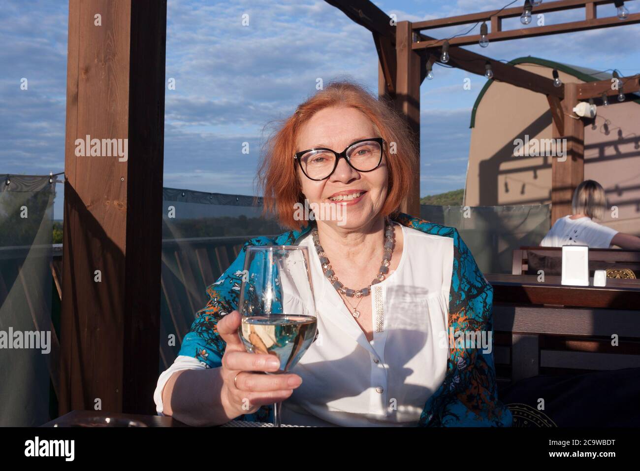 Una mujer de edad madura en una mesa de restaurante en un área abierta con una copa de vino blanco seco Foto de stock