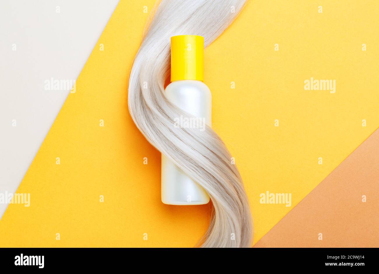 Shampoo botella de mascup hilo en el mechón de pelo rubio sobre fondo de color naranja. Champú de botella amarilla. Espacio de copia plano. Cosméticos para el cuidado del cabello Foto de stock