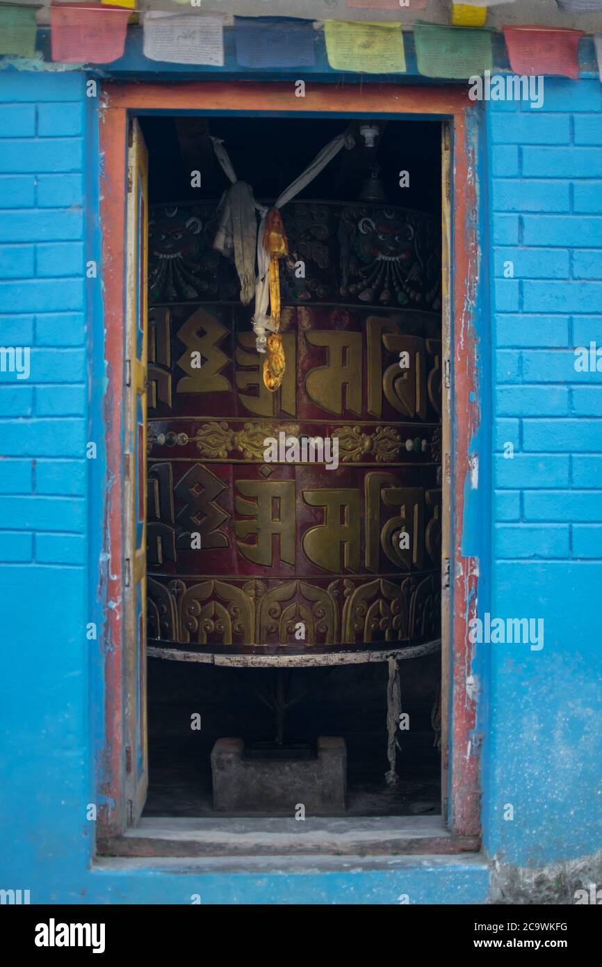 Enorme rueda de oración tibetana dentro de una casa con banderas de oración budista colgadas Foto de stock