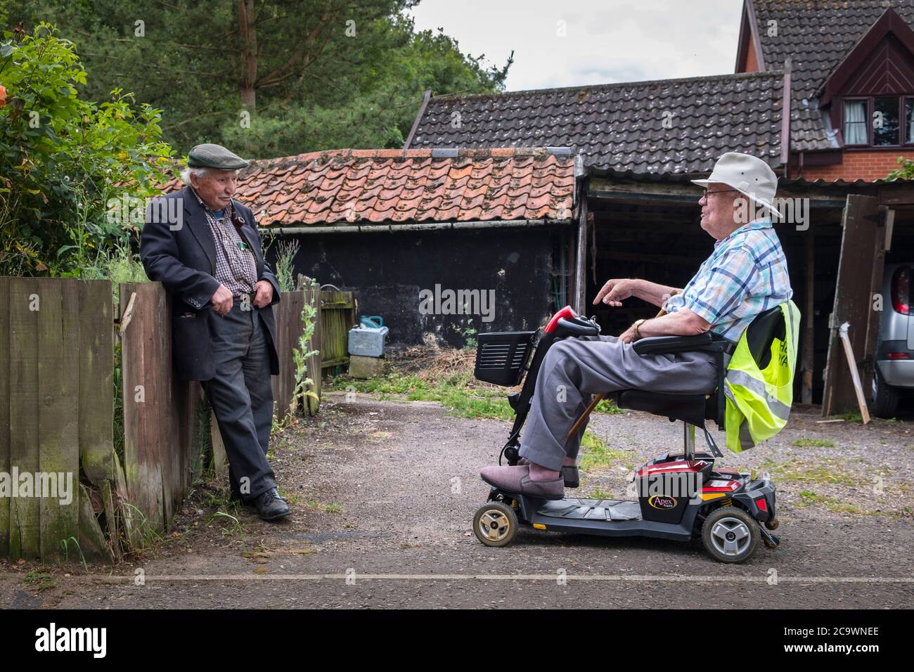 Dos hombres mayores charlando, uno está en una scooter de movilidad. Suffolk Village, Reino Unido. Foto de stock
