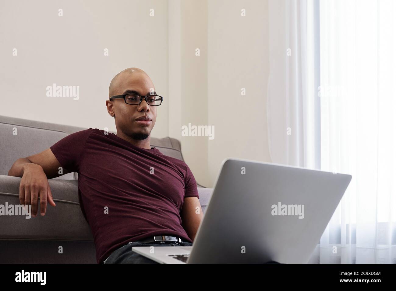 Hermoso joven calvo Negro hombre en vasos sentado en el suelo en la sala de  estar y disfrutar viendo un nuevo episodio de la serie de televisión  Fotografía de stock - Alamy