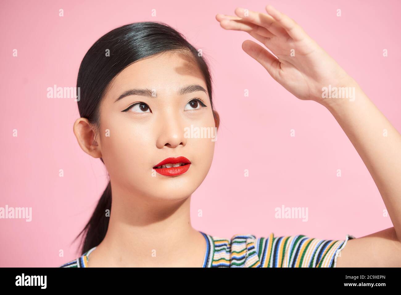 Mujer asiática hermosa joven asustado de sol aislado sobre fondo de color rosa. Concepto de cuidado de la piel para el verano y protección para la piel de los rayos UV del sol Foto de stock