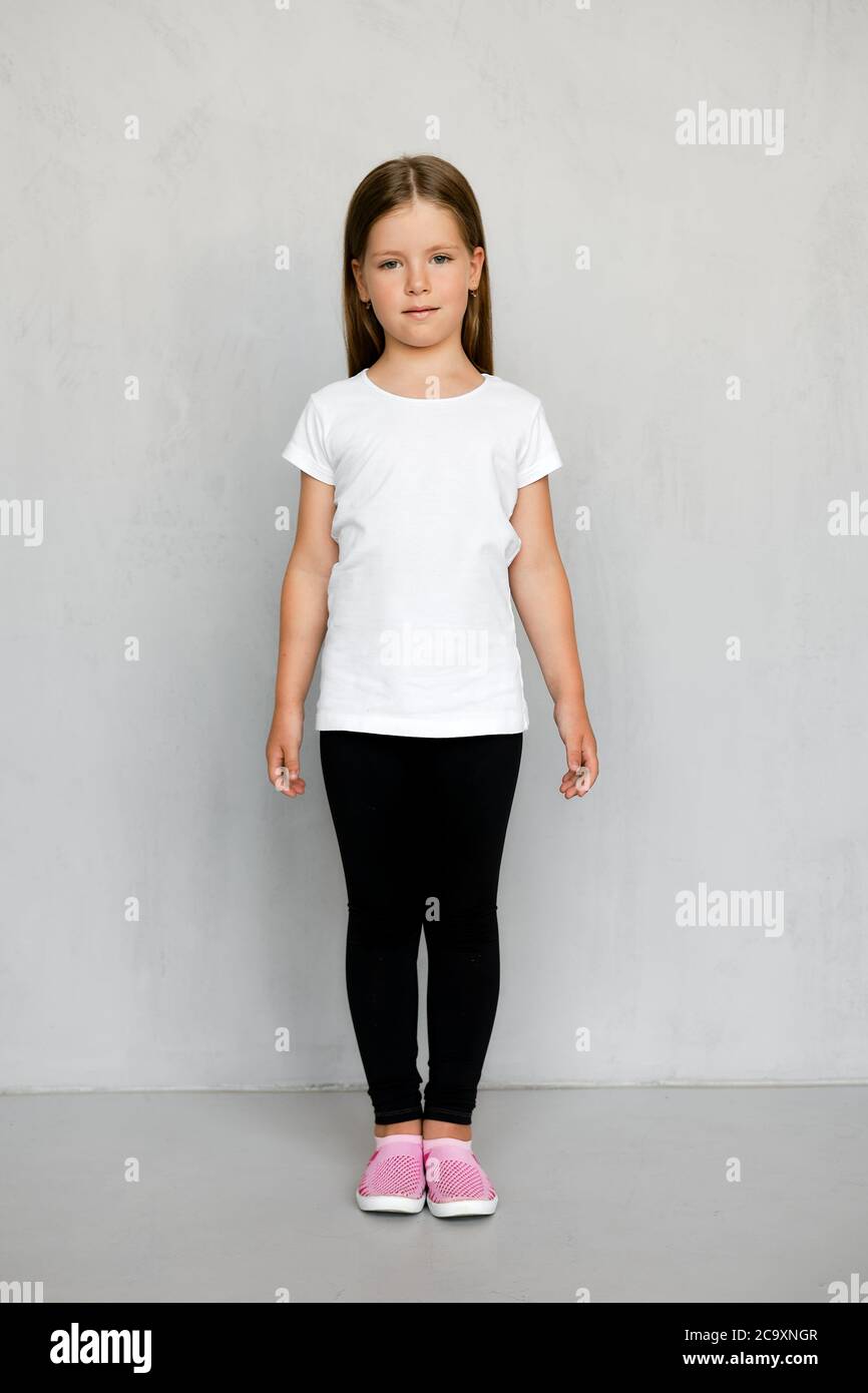 Lindo niño pequeño con pelo largo en camiseta blanca y pantalones de  chándal negro posando Fotografía de stock - Alamy