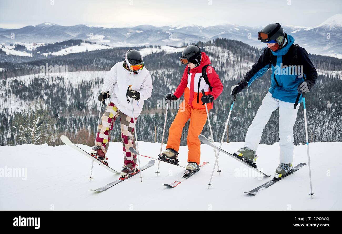 Longitud completa de tres esquiadores esquiando en las montañas. Mujer encantadora y dos hombres de pie en una colina cubierta de nieve mientras corres por la pendiente. Concepto de actividades deportivas de invierno y amistad. Foto de stock
