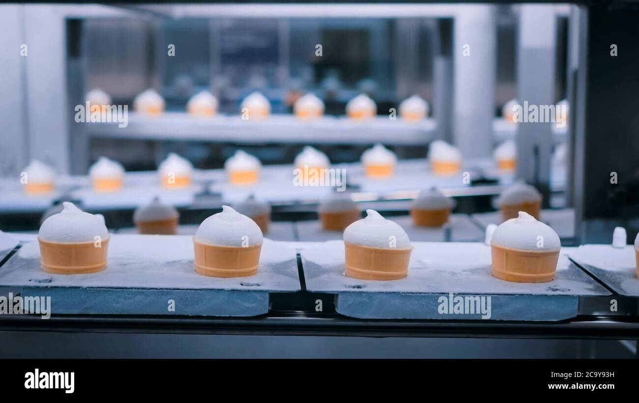 Línea de producción automática de helado - cinta transportadora con conos de helado en la moderna fábrica de procesamiento de alimentos. Industria láctea alimentaria, fabricación Foto de stock