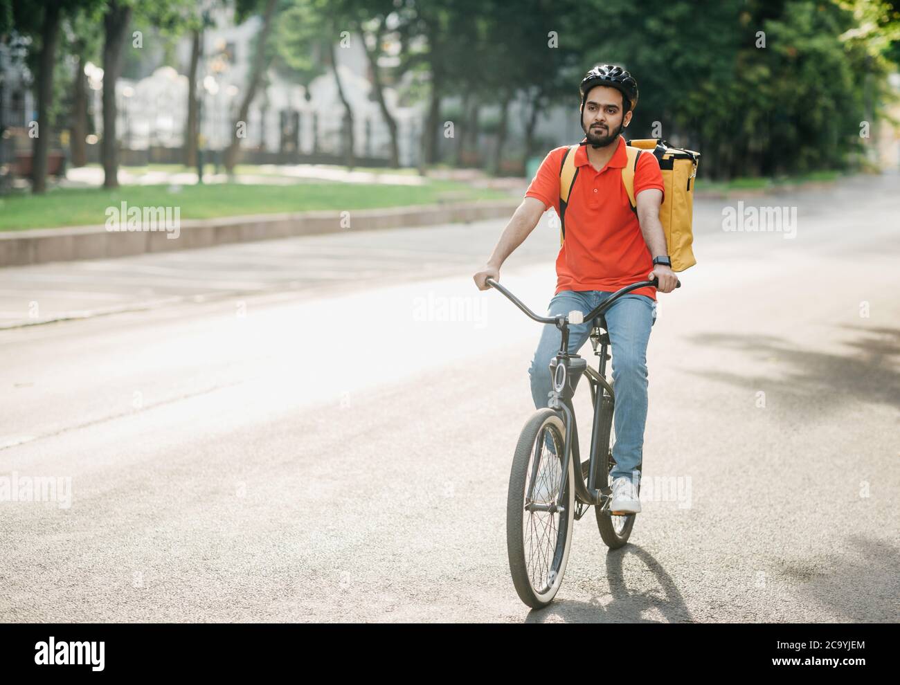 Entrega moderna en la ciudad. Hombre joven en casco con bolso paseos en bicicleta Foto de stock