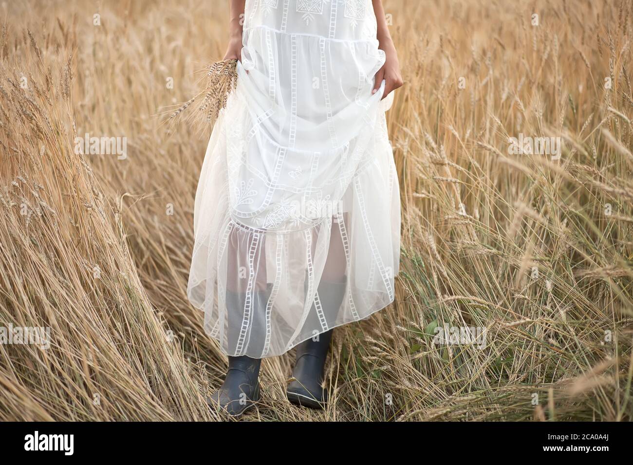 Mujer joven de pie en los campos de trigo con un vestido blanco y botas  negras. Boda en un estilo rústico Fotografía de stock - Alamy