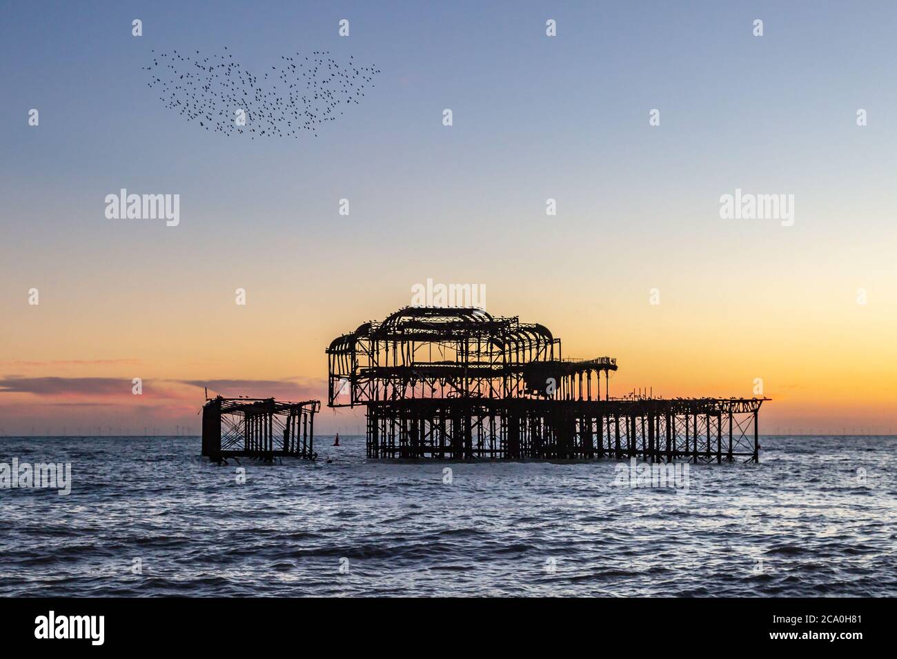 Una Murmuración en forma de corazón de los Starlings sobre el Old West Pier de Brighton, al atardecer Foto de stock