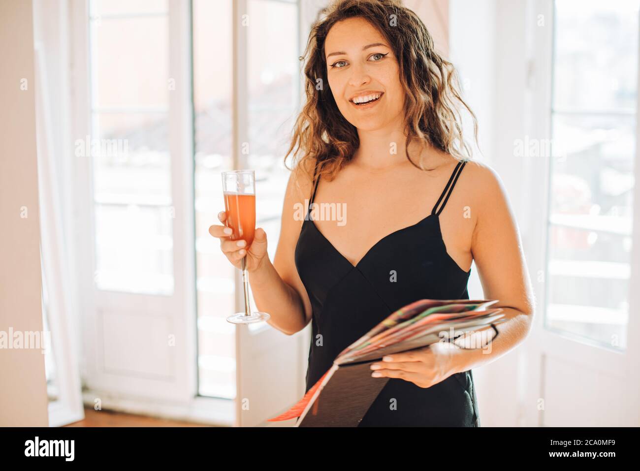 Mujer en vestido negro con copa de vino y álbum mirando la cámara Foto de stock