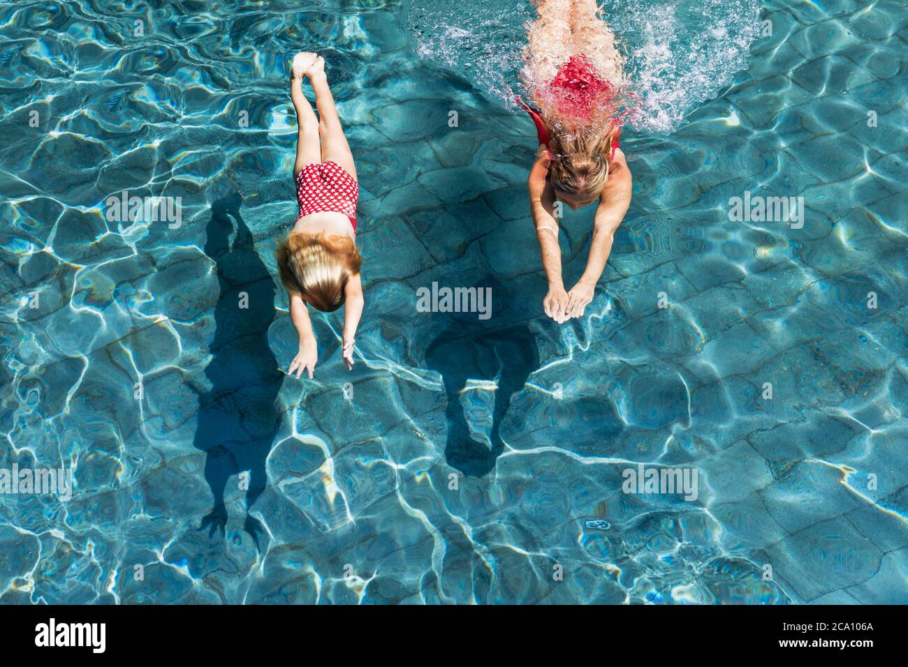 Feliz familia en la piscina. Niño con mujer joven nadar, bucear en la piscina con diversión - saltar profundamente bajo el agua. Estilo de vida saludable, gente deportes acuáticos Foto de stock