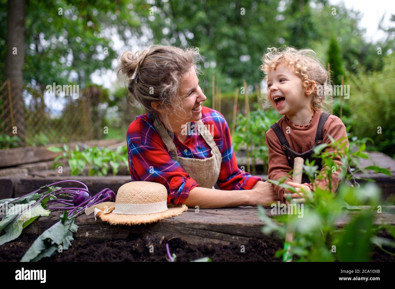 Madre con hija pequeña que cultiva un huerto en la granja, cultivando verduras orgánicas. Foto de stock