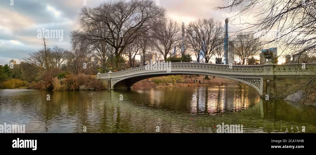 El puente de proa en el parque central, la ciudad de Nueva York luz del día vista con reflexión en el agua, las líneas del cielo, las nubes y los árboles Foto de stock