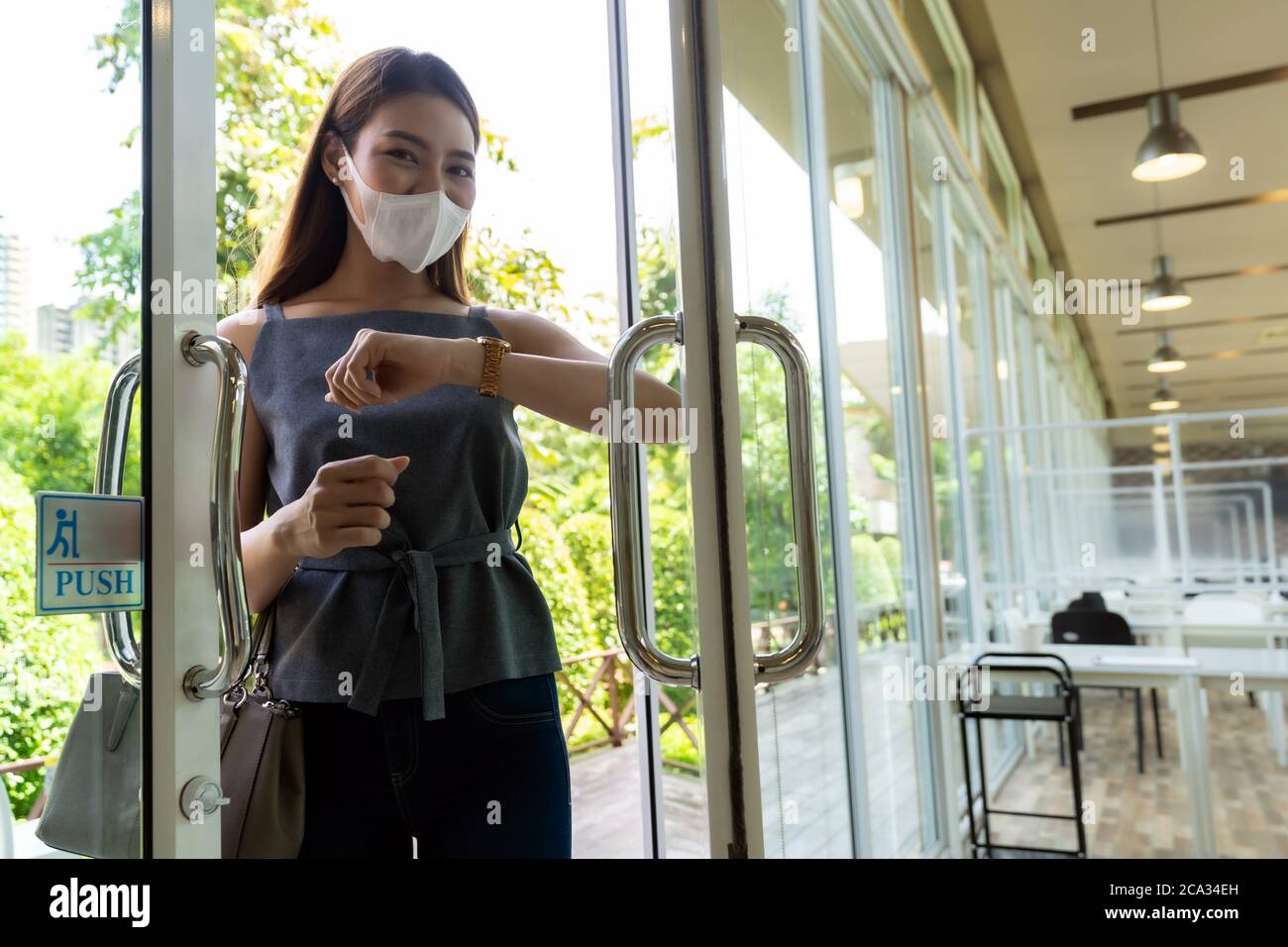 Retrato de una atractiva mujer asiática usando el codo para empujar la puerta del restaurante abierta para reducir el contacto de la mano en el lugar público para reducir la posibilidad de infección por Foto de stock