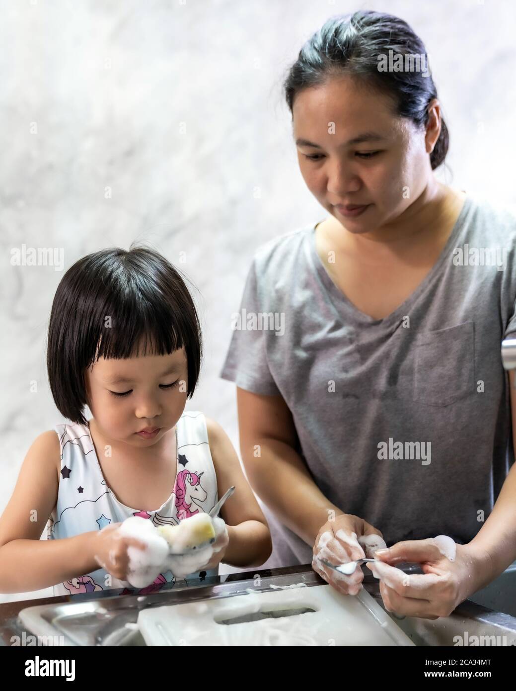 Niña asiática lavando plato y vajilla con su mamá, las tareas domésticas para el niño hacen la función ejecutiva para el niño. Trabajo en casa para niños estilo de vida y familia Foto de stock