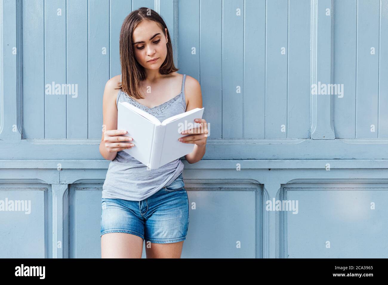Niña leyendo un libro sobre fondo gris azulado. Foto de stock