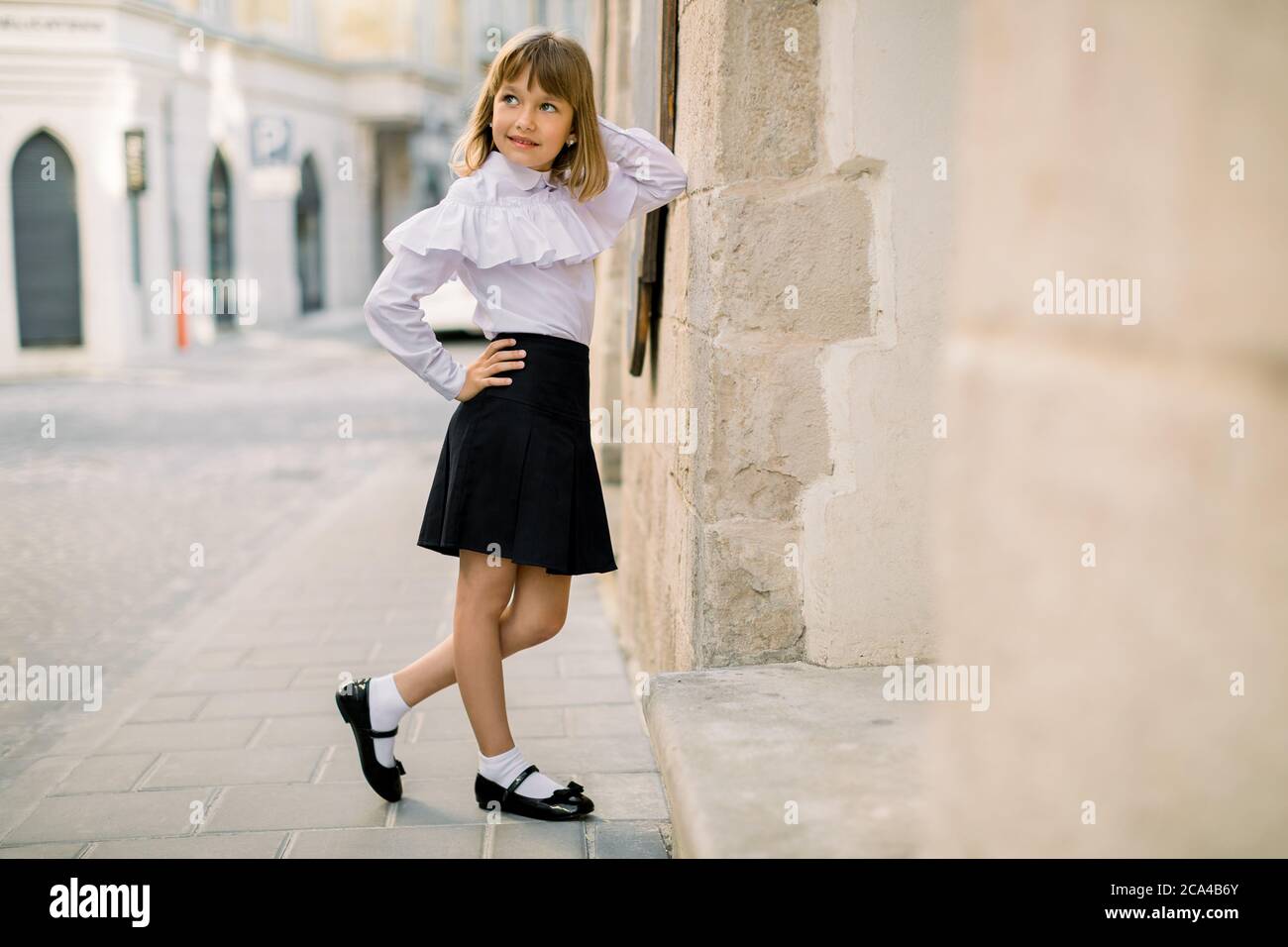 Retrato de moda libre de encantadora niña en blusa blanca y falda negra, posando apoyado en la pared hermoso edificio de la antigua en la antigüedad Fotografía de