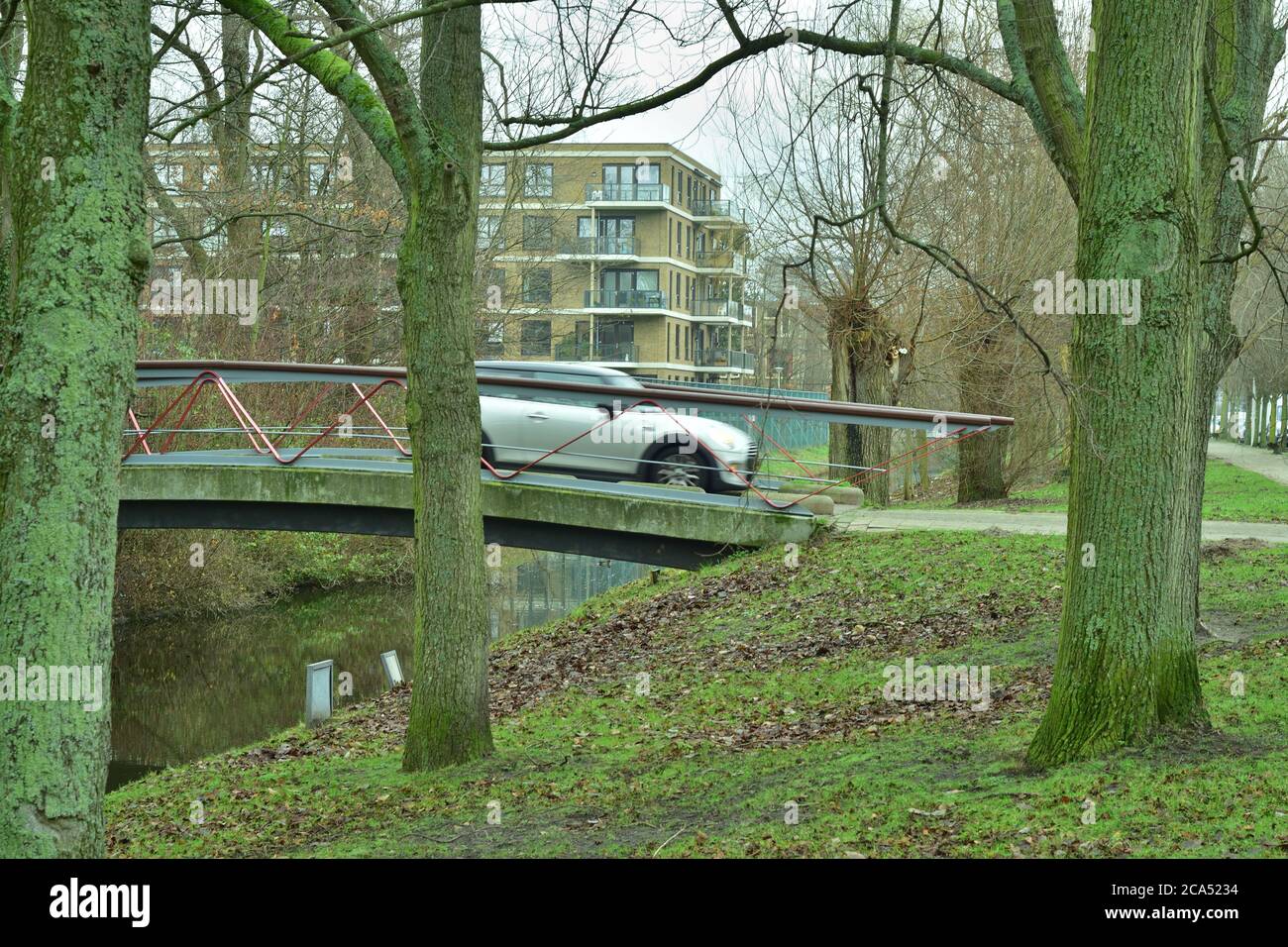Un coche en movimiento conduce sobre el puente del canal a las casas residenciales y los árboles. Primavera. Foto de stock